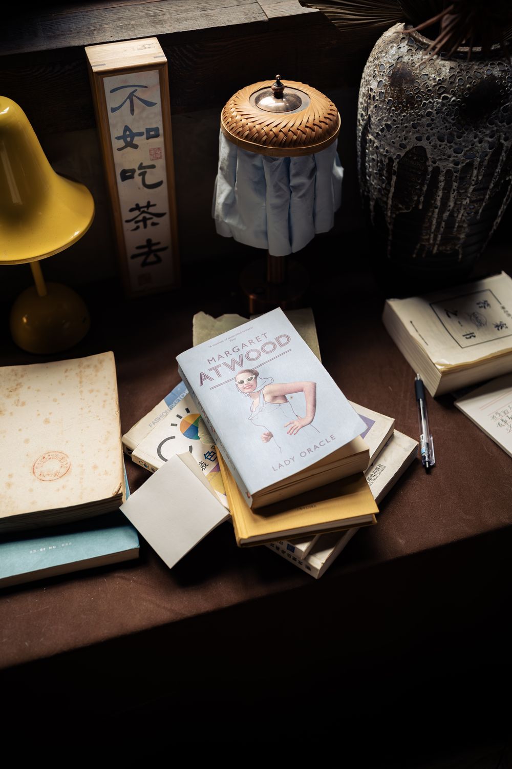 Warm still life of stacked books, lamps, and a calligraphy sign on a wooden desk