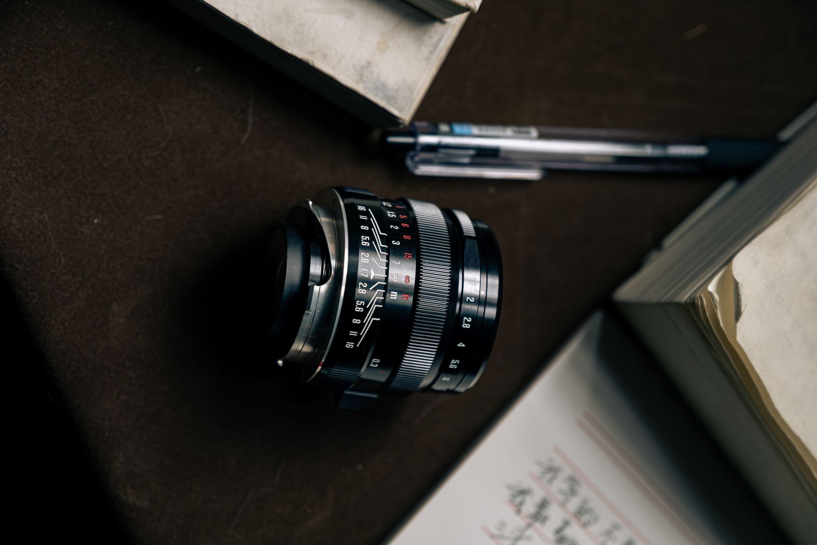 Top-down view of the compact lens on a desk beside a pen and books