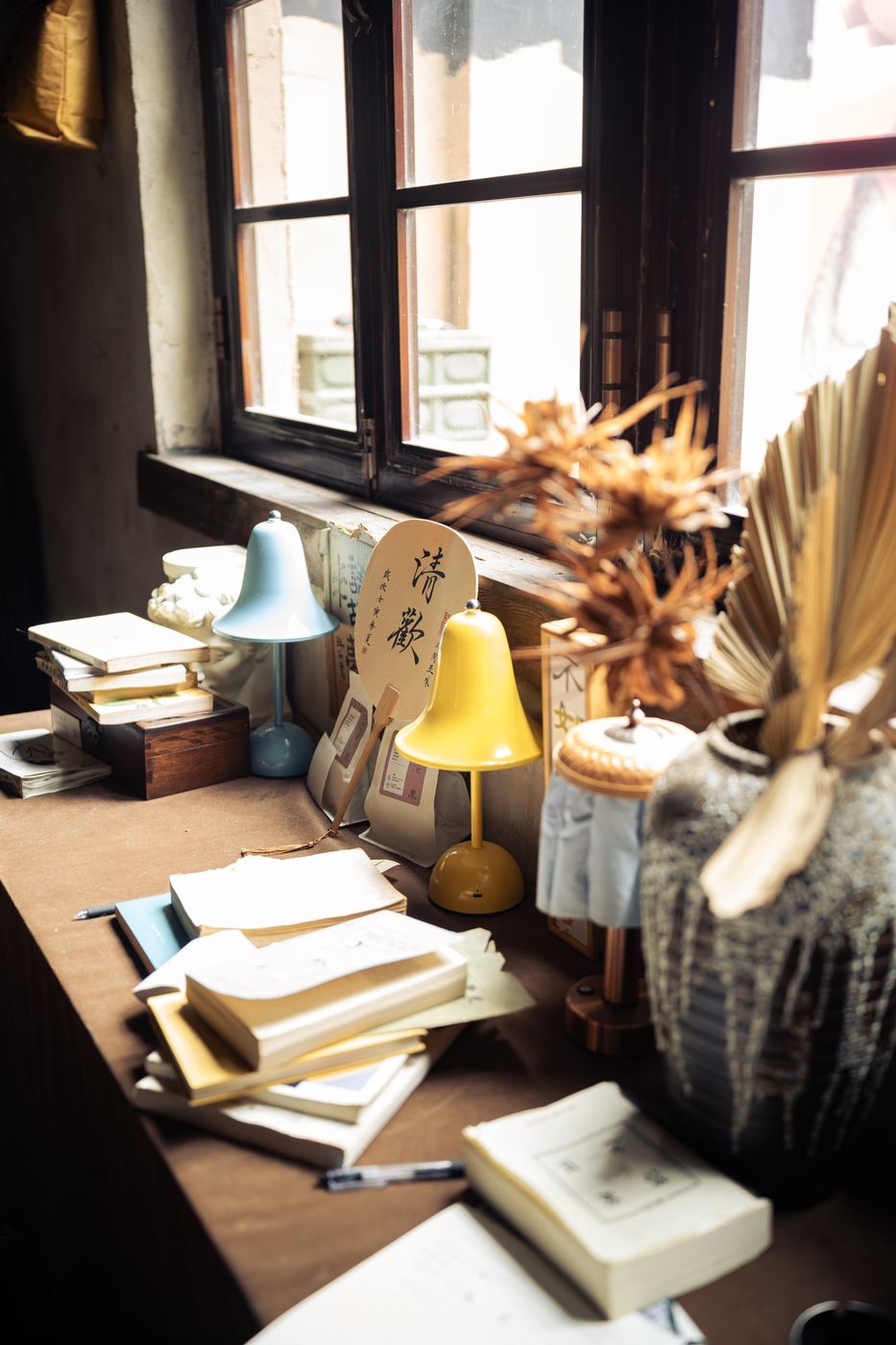 Sunlit desk with books and dried flowers by a window