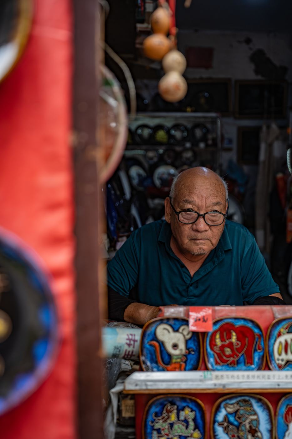 Elderly mask painter seated at his stall behind rows of painted opera masks