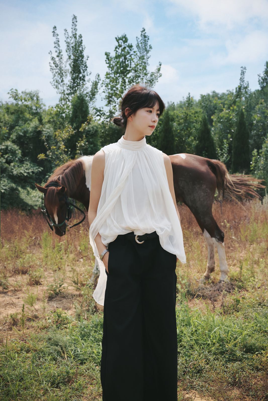 Portrait of a woman standing beside a horse in a summer field, shot at 35mm
